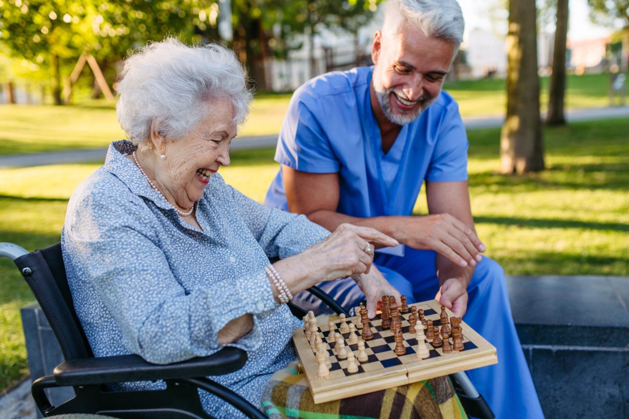 Senior playing chess outdoors with a caregiver