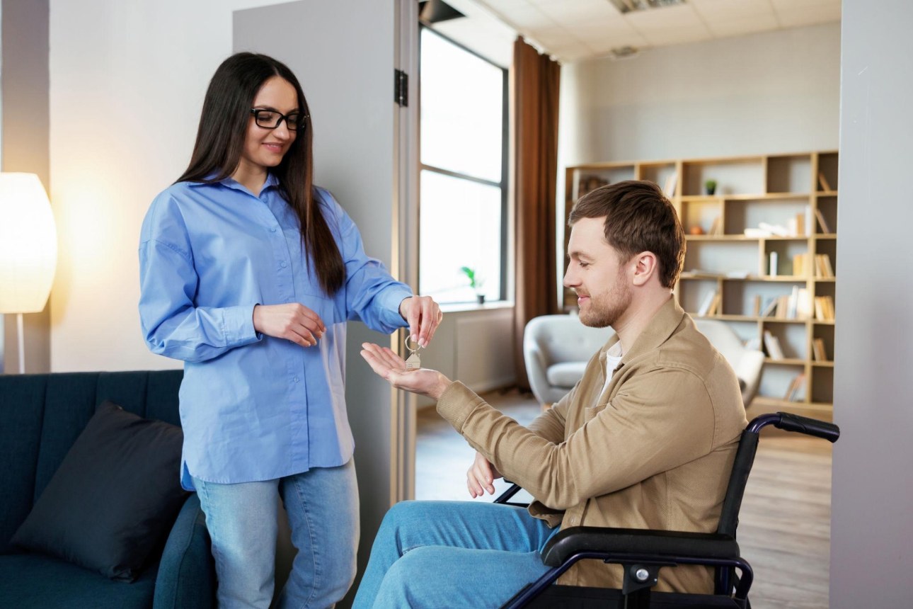 Woman handing house keys to a man in a wheelchair